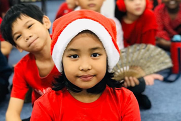 A girl from the best international school in Selangor is wearing a red shirt and a santa hat.
